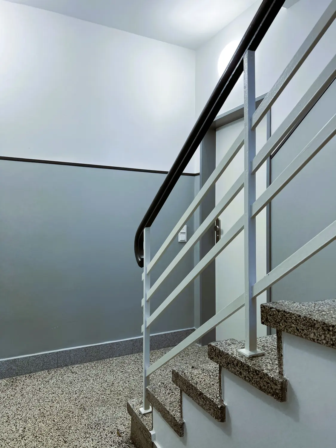 Fierle Baubetreuung – eine Treppe mit schwarzem Handlauf und weißem Metallgeländer