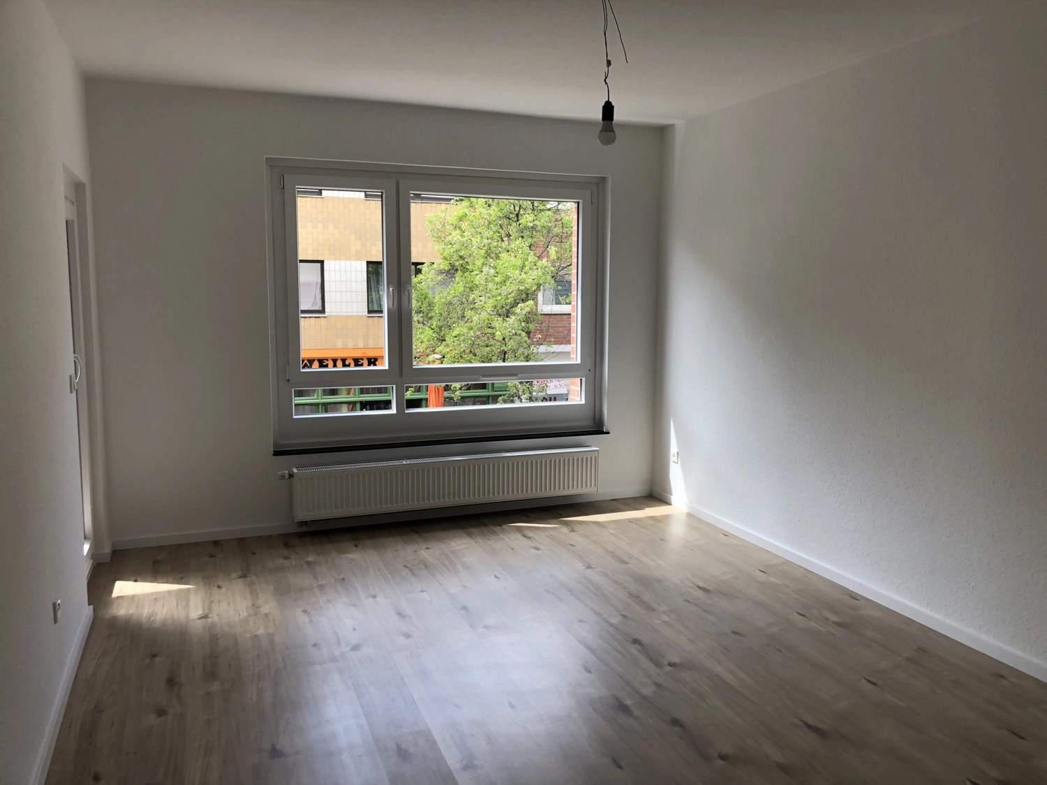 Fierle Baubetreuung – ein leerer Raum mit hellem Holzboden, weißen Wänden und einem großen Fenster